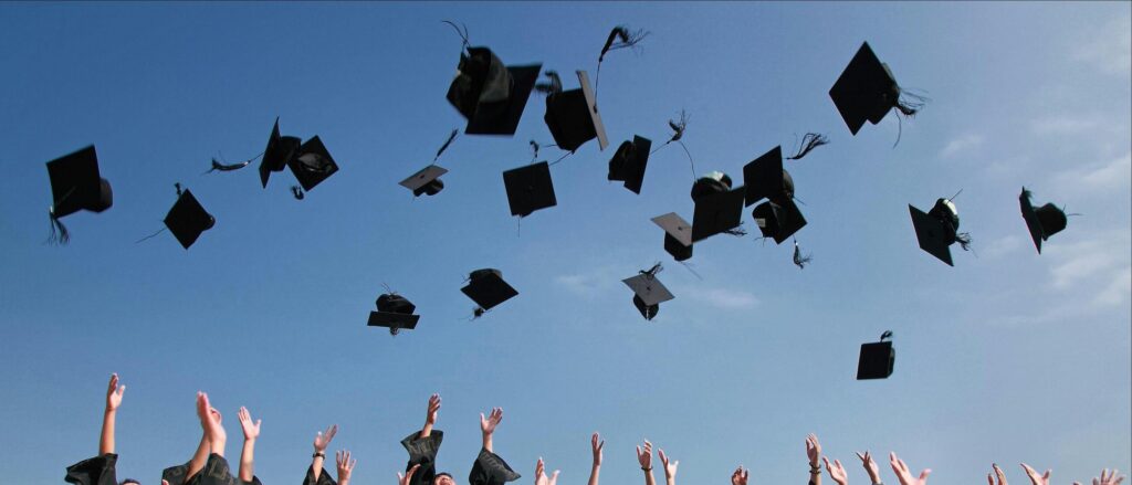 Group of graduates celebrating by throwing caps in the air during a sunny day.